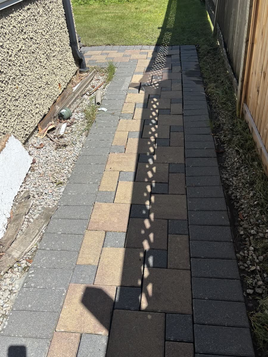 Clean multi-colour brick paver path beside a fence