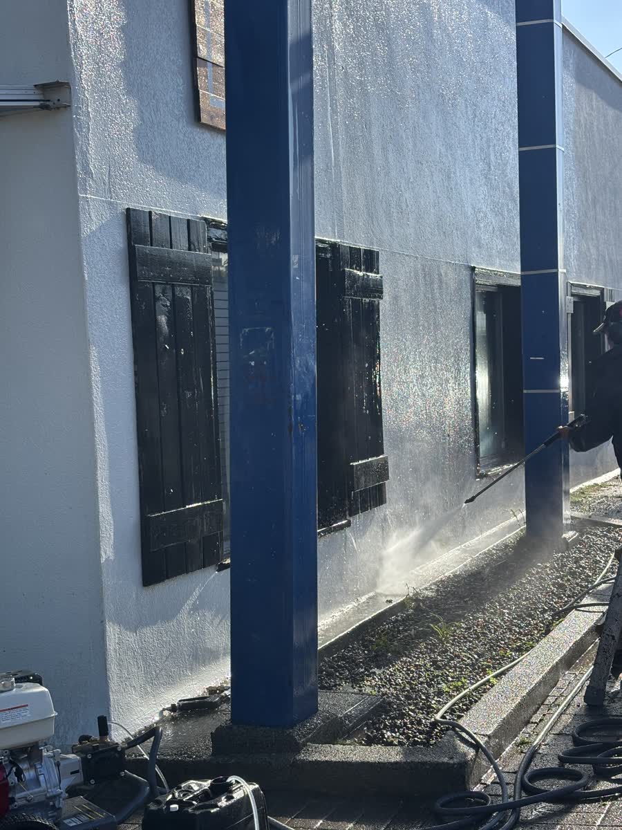 Worker soft washing a stucco wall with low pressure spray